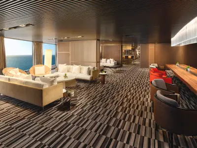 Umfassender Blick in die stilvolle, helle Lounge der Norwegian Viva mit grossen Fenstern zum Meer, komfortablen Sofas, Designerstuehlen und einer Bar im Hintergrund.