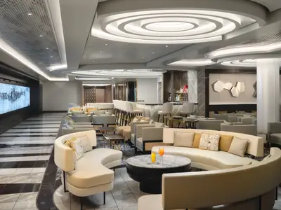 Die Metropolitan Bar an Bord der Norwegian Viva, eine stilvolle Lounge mit einer langen Bar, beigen Sofas, Sesseln, runden Deckenleuchten und moderner Wandkunst.