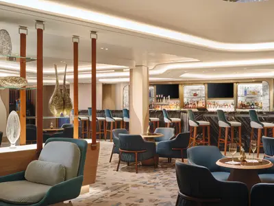 Die Penrose Bar an Bord der Norwegian Viva. Moderne Bar mit dunklem Marmortresen, blauen Hockern, Flaschenregalen. Blaue Lounge-Sessel, Tische und Glasvasen.
