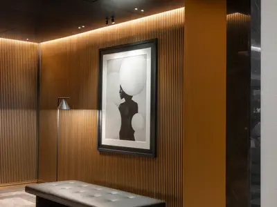 Ein stilvoller Innenraum an Bord der Norwegian Viva mit vertikalen Holzlamellenwänden, indirekter Beleuchtung und einem prominenten Schwarz-Weiß-Kunstwerk. Eine schlanke Stehlampe steht links von dem Bild.