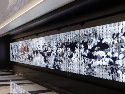 Eine lange, hochauflösende digitale Kunstwand an Bord der Norwegian Viva zeigt Schwärme von leuchtenden, silbrigen Schmetterlingen vor dunklem Hintergrund.