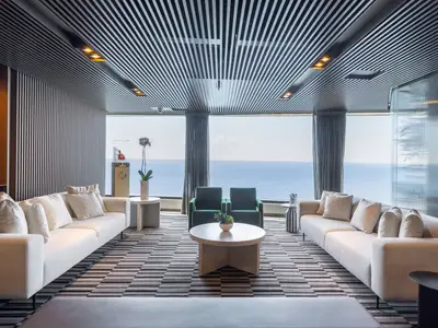 Eine geräumige, elegante Lounge an Bord der Norwegian Viva mit raumhohen Fenstern und Meerblick. Weisse Sofas, eine gestreifte Decke und dunkelgrüne Sessel schaffen eine entspannte Atmosphäre.