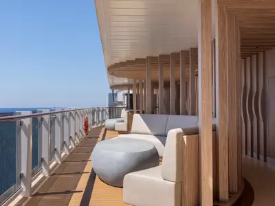 Panoramablick auf die offene Lounge 'La Terrazza' an Bord der Norwegian Viva. Moderne Sofas und Tische unter einer stilvollen Holzüberdachung mit Blick auf das blaue Meer und den Himmel.