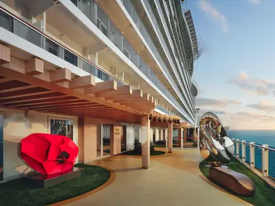 Eine elegante Promenade an Bord der Norwegian Viva mit modernen Kunstskulpturen, Holzelementen und Blick auf das weite Meer bei Sonnenuntergang.