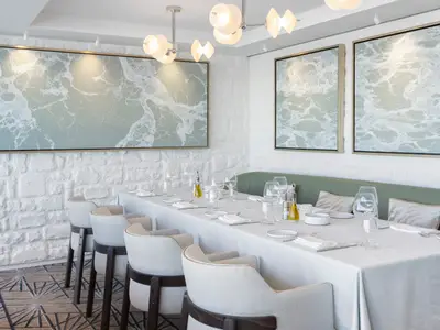Elegantes Restaurant an Bord der Norwegian Viva mit langer, weiß gedeckter Tafel, grauen Stühlen und grüner Sitzbank. Weiße Ziegelwände mit großformatigen, abstrakten Wellenbildern.