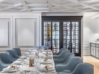 Ein festlich gedeckter Esstisch mit blaugrauen Stühlen in einem gehobenen Restaurant an Bord der Norwegian Viva. Im Hintergrund sind zwei grosse, beleuchtete Wein-Displays mit vielen Flaschen Wein und Champagner zu sehen, die die elegante Atmosphäre unterstreichen.