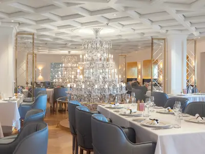 Das luxuriöse Le Bistro Restaurant an Bord der Norwegian Viva. Große Kristall-Kronleuchter, gedeckte Tische, blaugraue Stühle und goldene Wandakzente prägen den hellen Raum.