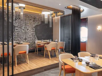 Restaurant an Bord der Norwegian Viva. Gedeckte Tische mit hellen Stühlen, orangen Akzenten und einer grossen, abstrakten Wandmalerei.