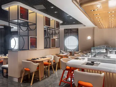 Ein elegantes Restaurant an Bord der Norwegian Viva. Moderne Tische, orange Stühle, eine Theke und dekorative Raumteiler mit Kunstwerken schaffen eine stilvolle Atmosphäre.