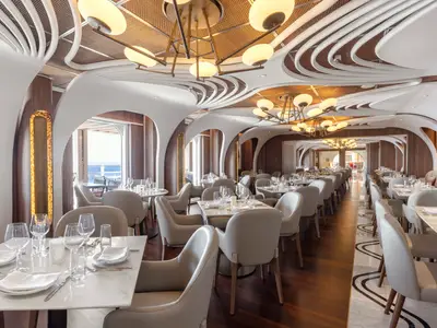 Elegantes Restaurant Onda auf der Norwegian Viva. Moderne Tische, Stühle, geschwungene Decken und Meerblick durch Fenster prägen den Raum.