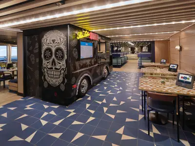 Restaurant Latin Quarter an Bord der Norwegian Viva. Ein Food Truck mit Zuckerschädel-Design, blaue Fliesen, gemusterte Tische mit Tablets.