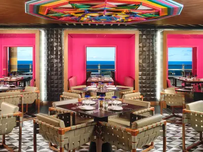 Das Spezialitätenrestaurant Los Lobos an Bord der Norwegian Viva. Moderne Einrichtung mit leuchtend pinken Wänden, komfortablen Sitzgelegenheiten, gedeckten Tischen und weitem Meerblick.