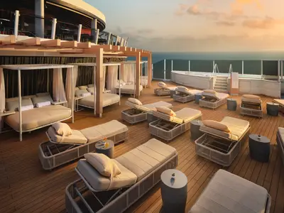 Blick auf das obere Außendeck der Norwegian Viva bei Sonnenuntergang, mit zahlreichen modernen Lounge-Liegen, mehreren privaten Cabanas mit Vorhängen und einem Whirlpool am Rand mit Blick auf das Meer.