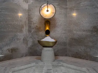 Eine goldene Zapfstelle spendet grobes Eis in eine goldene Schale. Die Installation steht auf einem hellen Steinsockel vor marmorierten Wänden im Spa der Norwegian Viva.