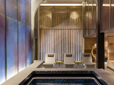 Elegante Spa-Oase an Bord der Norwegian Viva. Moderne Liegen vor stilvoller Wand aus Holz und Metall. Thermalbecken und beleuchtete blau-violette Wand.