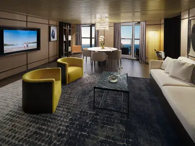Innenansicht einer luxuriösen Suite an Bord der Norwegian Viva. Ein Wohnbereich mit zwei gelben Sesseln und einem langen Sofa, ein Essbereich mit rundem Tisch und Stühlen, sowie große Fenster mit Meerblick sind zu sehen.