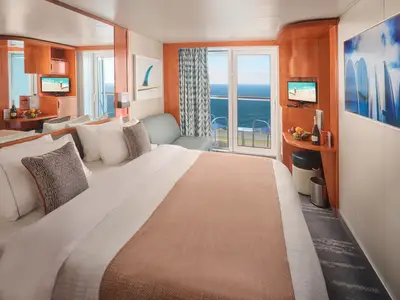 Eine helle und moderne Balkonkabine an Bord der Pride of America mit einem Doppelbett, einem kleinen Sofa, einem TV und einem Balkon mit Blick auf das offene Meer.