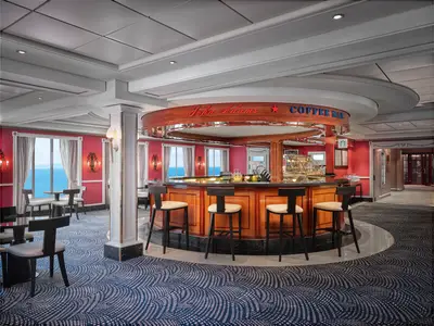 Blick in die John Adams Coffee Bar an Bord der Pride of America, eine stilvolle Lounge mit roter Tapete und Meerblick. Eine runde Holzbar und bequeme Stühle laden zum Verweilen ein.