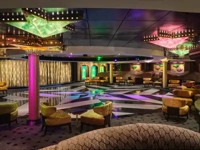 Die farbenfrohe Mardi Gras Lounge an Bord der Pride of America. Die Tanzfläche hat ein schwarz-weißes Sternenmuster. Auffällige goldene Vorhänge und diverse Sitzgruppen unterstreichen das Ambiente.