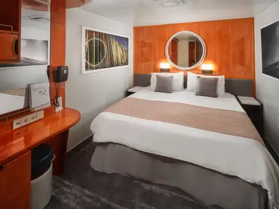 Eine helle Innenkabine an Bord der Pride of America mit einem Doppelbett, zwei Nachttischen, einem Schreibtisch und einem Spiegel. Die Wände sind weiß und orange getäfelt. Geräumige Kabine.
