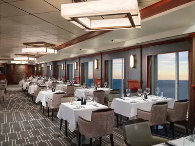 Elegantes Restaurant "Cagney's Steakhouse" an Bord der Pride of America mit fertig gedeckten Tischen und großen Fenstern mit Meerblick bei Sonnenuntergang.