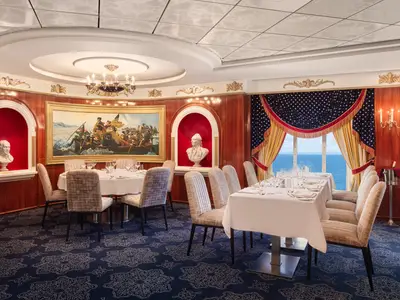 Das Spezialitätenrestaurant Liberty an Bord der Pride of America. Dunkles Holz, Büsten, ein Gemälde, patriotische Vorhänge und elegant gedeckte Tische. Fenster bieten Meerblick.