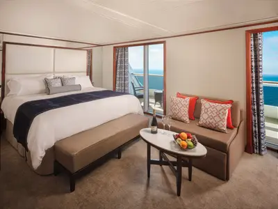Geräumige Suite mit komfortablem Doppelbett, Balkon mit Meerblick und gemütlicher Sitzecke mit frischem Obst an Bord der Pride of America. Die Einrichtung ist modern und hell.