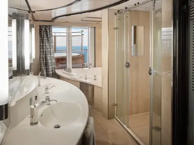 Badezimmer einer Suite auf der Pride of America. Mit Doppelwaschbecken, grosser Badewanne, Glasdusche und Fensterblick auf privaten Balkon mit Whirlpool sowie das weite Meer.