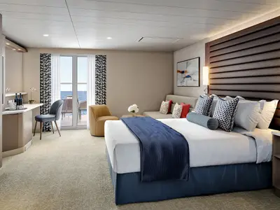 Geräumige Mini-Suite mit Doppelbett, Sofa, Schreibtisch und Balkon mit Meerblick an Bord der Pride of America. Modernes Design mit blauen Akzenten und Tageslicht.