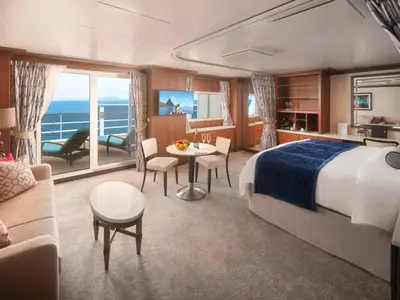 Geräumige Penthouse-Suite an Bord der Pride of America mit Doppelbett, Essbereich, Sofa, Beistelltisch und privatem Balkon mit Meerblick.