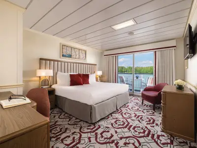 Kabine an Bord der American Splendor mit großem Bett, Schreibtisch und Balkon. Der Blick geht auf den Fluss und bewaldete Ufer. Ein rot-grauer Teppich ist zu sehen.