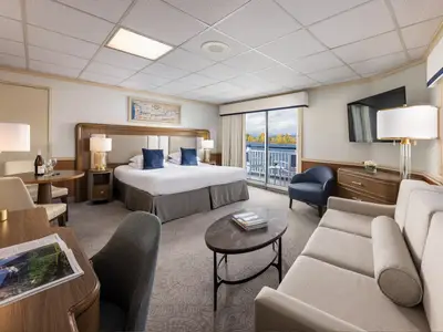 Blick in eine geräumige Suite der American Splendor. Das Zimmer verfügt über ein Doppelbett, Sofa, Esstisch, Schreibtisch und einen Balkon mit Flussblick auf herbstliche Ufer.
