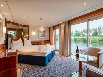 Die Kabine der Belvedere bietet ein Doppelbett, einen Sitzbereich mit Wein am Fenster und Flussblick. Die helle Einrichtung mit Holz und blauem Teppich wirkt einladend.