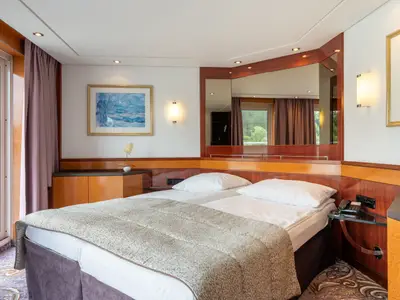 Komfortable Kabine auf dem Flusskreuzfahrtschiff Belvedere. Zwei Betten, Glastür mit Flussblick links. Holzvertäfelung, Spiegel und Kunstwerke zieren den Raum. Ein Telefon steht neben dem Bett.