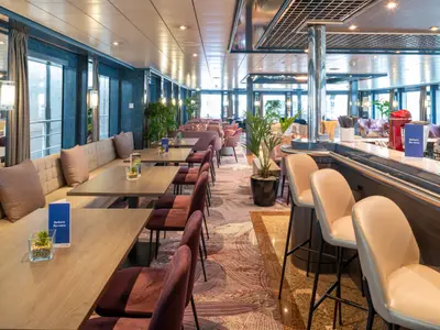 Lounge- und Barbereich des Flusskreuzfahrtschiffs Belvedere mit Tischen, Bänken, Stühlen, Bar, Hockern und großen Fenstern.