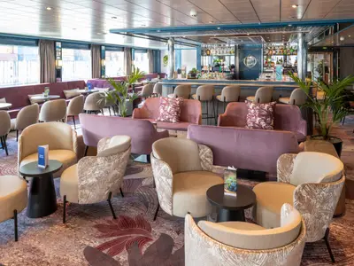 Die Lounge und Bar des Flusskreuzfahrtschiffs Belvedere ist stilvoll eingerichtet. Man sieht Sessel, Sofas und eine Bar mit Hockern in modernem Design.