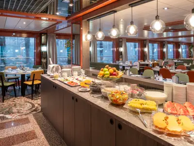 Reichhaltiges Frühstücksbuffet an Bord der Belvedere. Frisches Obst, Müsli und Speisen auf dem Tresen. Heller Speisesaal mit gedeckten Tischen und großen Fenstern.