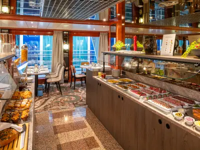Einladender Buffetbereich auf dem Flusskreuzfahrtschiff Belvedere. Es sind verschiedene Speisen wie Backwaren, Aufschnitt und warme Gerichte an einer Theke angerichtet. Im Hintergrund sind Tische und große Fenster mit Blick nach draußen zu sehen.