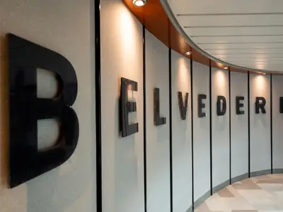Geschwungene Wand im Schiffsinneren mit großen, glänzenden schwarzen Buchstaben, die 'BELVEDERE' bilden. Warme Deckenstrahler beleuchten die helle, texturierte Wand.