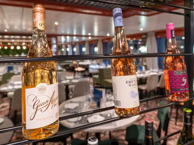 Drei Roséweinflaschen auf einem Regal. Im Hintergrund ein elegantes, unscharfes Restaurantambiente mit Tischen und warmer Beleuchtung.
