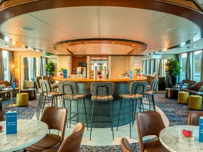 Blick in die Bar-Lounge der Bijou du Rhône. Zentrale Bar mit Hockern, Sitzgruppen und großen Fenstern. Flusslandschaft ist sichtbar.