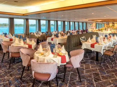 Ein Blick in den Speisesaal der Bijou du Rhône mit vielen gedeckten Tischen. Große Fensterfront mit Blick aufs Wasser. Elegante Einrichtung und Buffetbereich im Hintergrund.