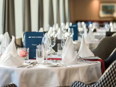 Festlich gedeckter Tisch im Restaurant der Bijou du Rhône. Darauf Gläser, Besteck, weiße Servietten und Menükarte. Weitere Tische und Fenster im Hintergrund.