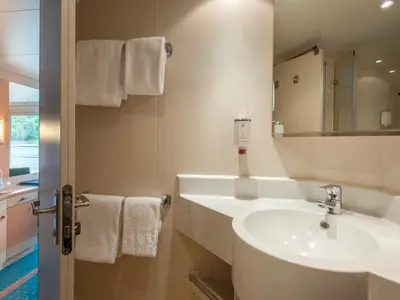 Badezimmer einer Kabine auf dem Flusskreuzfahrtschiff Bolero. Es zeigt Waschbecken, Spiegel, Handtücher und den Blick in den Wohnbereich mit Fensteraussicht.