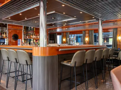 Der elegante Bar- und Loungebereich des Flusskreuzfahrtschiffs Bolero. Zu sehen sind der Tresen mit Barhockern, Flaschen und Zapfanlagen im Hintergrund sowie eine Fensterfront mit Ausblick.