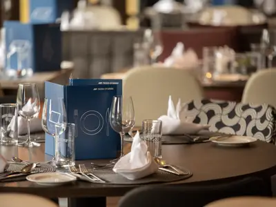 Gedeckter Tisch im Restaurant der nicko cruises Bolero. Blaue Menükarten, Gläser und Besteck im Vordergrund. Im unscharfen Hintergrund weitere Tische der Bolero.