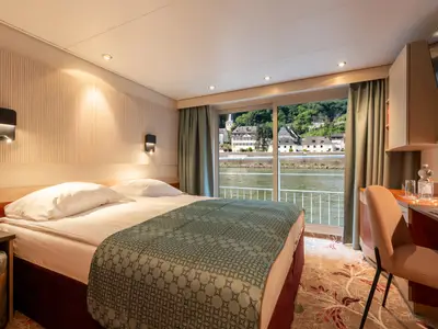 Moderne Kabine des Flusskreuzfahrtschiffs Celina: Doppelbett, Schreibtisch und großes Fenster. Panoramablick auf grüne Flusslandschaft und Uferstadt.