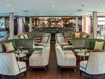 Die Lounge des Flusskreuzfahrtschiffs Douro Queen zeigt eine Bar mit Barkeeper und Sitzgruppen aus Sofas und Sesseln in Grün und Beige. Kleine Tische mit Blumen.