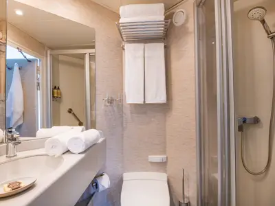 Modernes, helles Badezimmer einer Kabine auf der Douro Queen von nicko cruises. Mit Waschtisch, Spiegel, Toilette und Duschkabine, ausgestattet mit weißen Handtüchern.