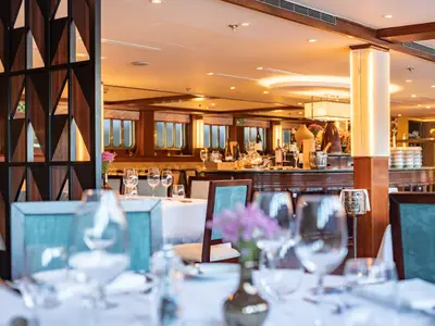 Das Restaurant der Douro Queen. Gedeckte Tische mit Gläsern, im Hintergrund eine Bar und ovale Schiffsfenster.